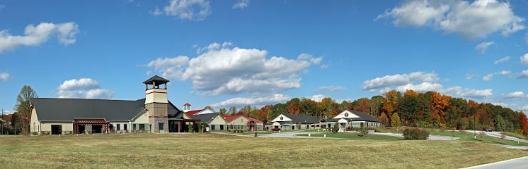 Apartments in for rent Farragut TN A large, modern building complex with a tower sits on a grassy field, surrounded by trees with autumn foliage under a partly cloudy sky. Anchor 934 Apartments in Biddle Farms Town Center