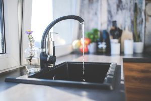 Apartments in Farragut Water flows from a modern faucet into a black sink in a sunlit kitchen, with a small vase of flowers and fruit on the counter.