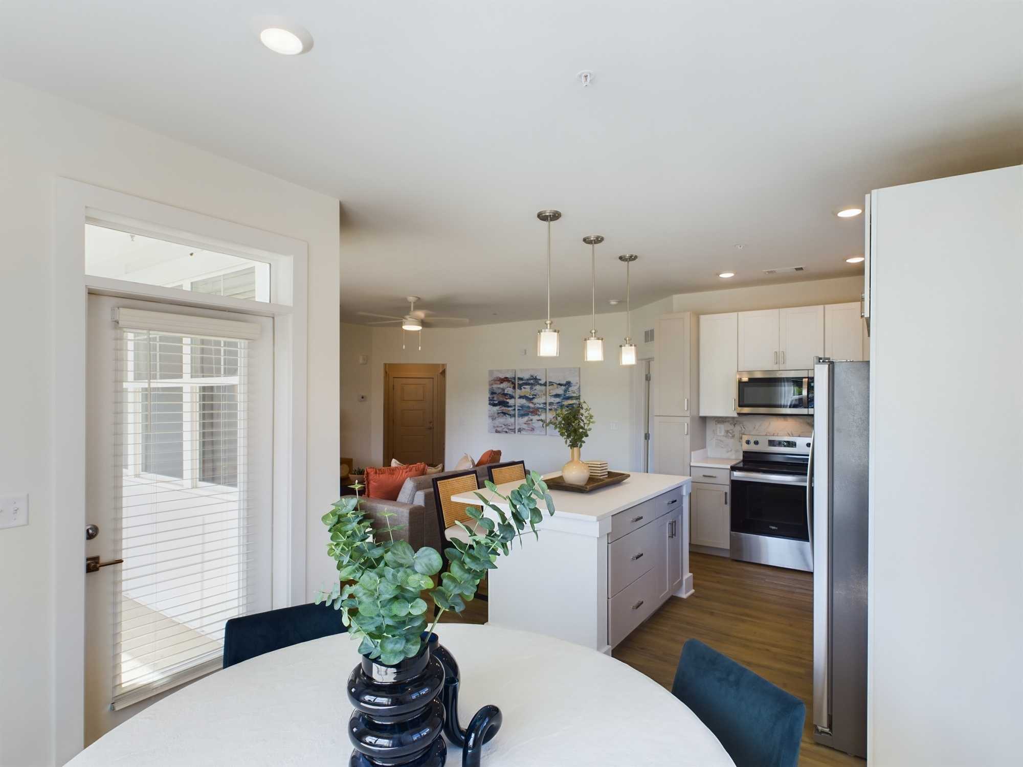 Apartments in Farragut Modern kitchen and dining area with white cabinetry, stainless steel appliances, an island with pendant lights, and a round table with a centerpiece. Adjacent living room contains a couch and artwork.