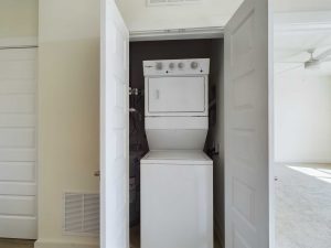 Apartments in Farragut A small laundry area in a rental property contains a stacked washer and dryer unit with white double doors open, revealing the appliances. The surrounding walls and door are white, creating a clean and efficient space perfect for apartment living.