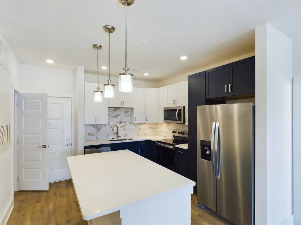Apartments in Farragut Modern kitchen with white and dark cabinetry, stainless steel appliances, and a central island. Features pendant lighting, wooden flooring, and marble backsplash. Perfect for rental properties or apartments with visible doors and windows.