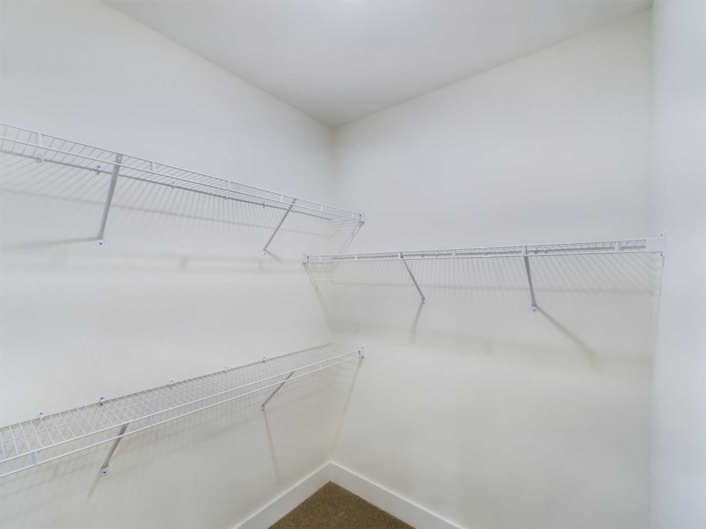 Apartments in Farragut Empty walk-in closet with three wire shelves installed on white walls. The floor is carpeted in a light brown color, perfect for organizing your belongings in rental properties or apartments.