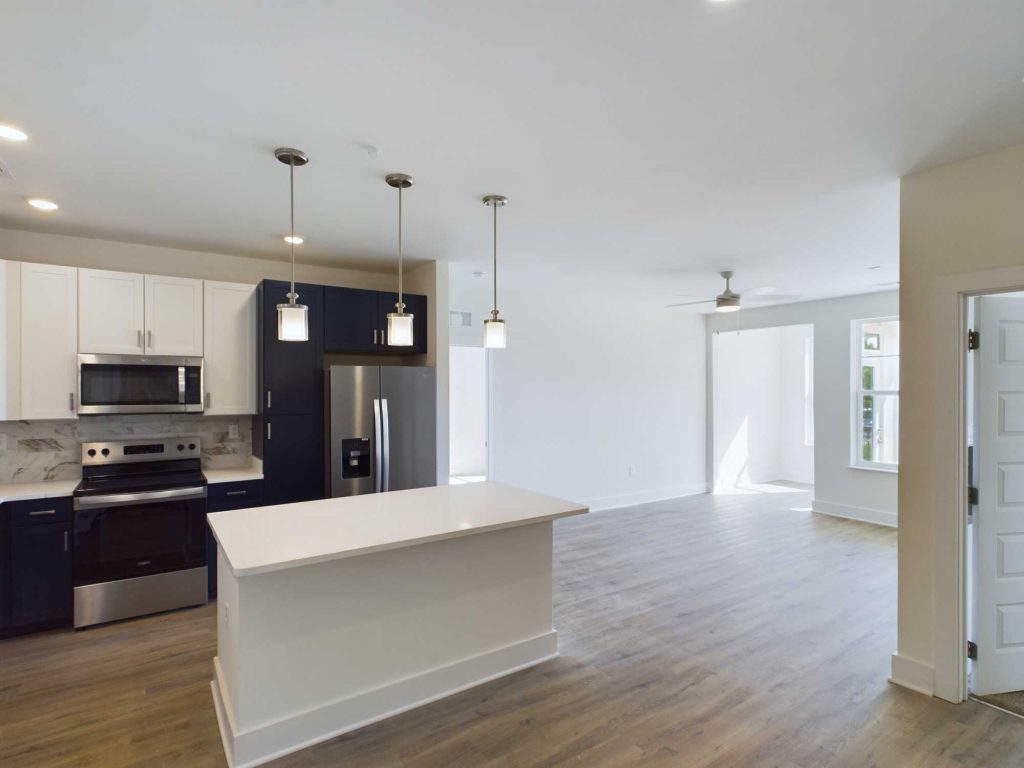 Apartments in Farragut Modern open-concept kitchen and living area in upscale rental units, featuring a central island with pendant lights, stainless steel appliances, white and dark cabinets, and a spacious adjoining room with large windows.