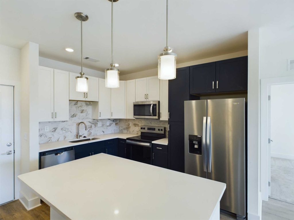 Apartments in Farragut Modern kitchen with white and dark cabinets, stainless steel appliances including a refrigerator and microwave, a center island with a white countertop, and three hanging pendant lights— ideal for those seeking stylish apartments for rent.