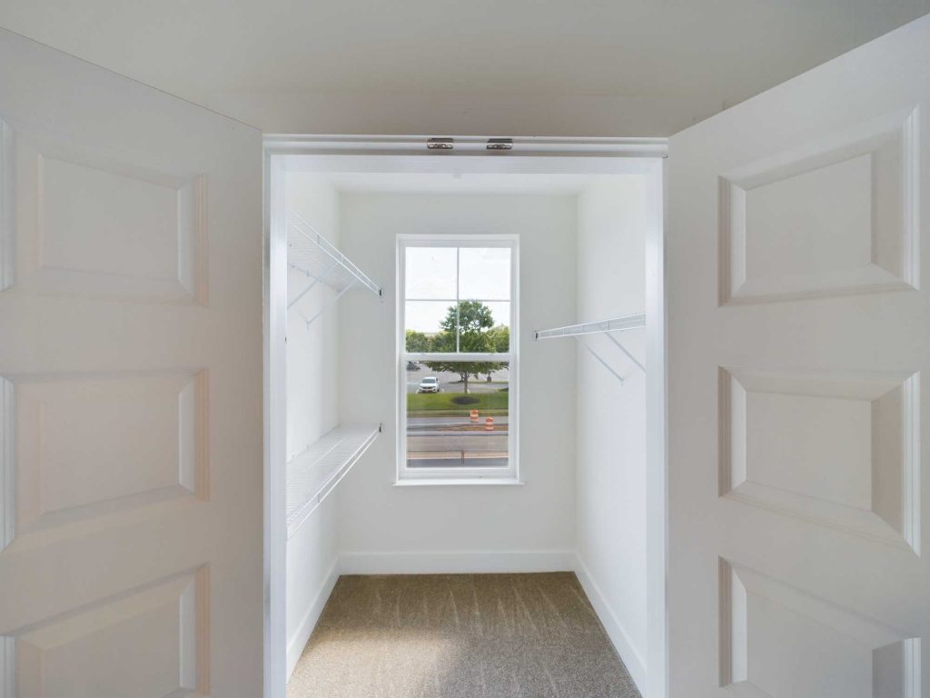Apartments in Farragut Open double doors reveal a walk-in closet with shelves on both sides, beige carpet, and a window providing natural light—an ideal feature often highlighted in top-tier rental apartments.