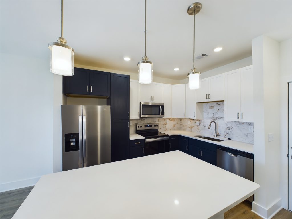 Apartments in for rent Farragut TN Modern kitchen in one of the charming apartments for rent in Farragut, Tennessee, featuring white and navy blue cabinets, stainless steel appliances, a marble backsplash, and pendant lights over a large island. Anchor 934 Apartments in Biddle Farms Town Center