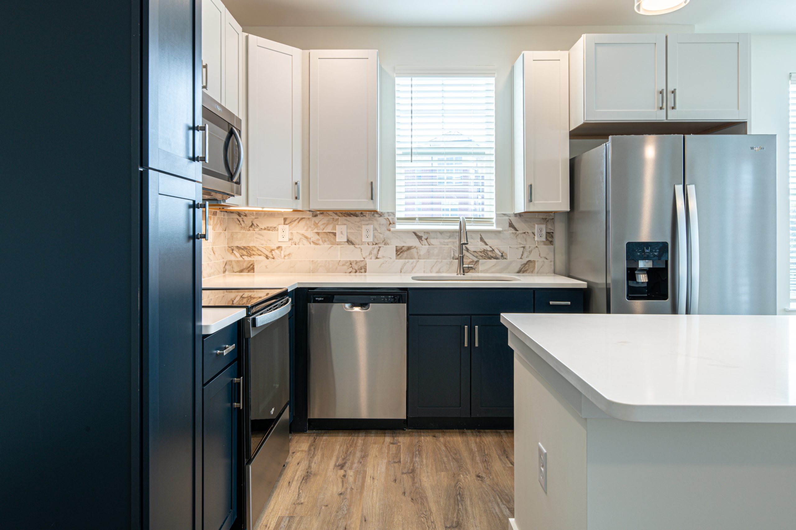 Apartments in for rent Farragut TN Modern kitchen with stainless steel appliances, white and dark cabinets, marble backsplash, and wooden floor. Anchor 934 Apartments in Biddle Farms Town Center