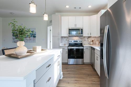 Apartments in for rent Farragut TN Modern kitchen with white cabinets, stainless steel appliances, and wood flooring. Island with decorative tray and plants. Hanging pendant lights illuminate the space. Anchor 934 Apartments in Biddle Farms Town Center