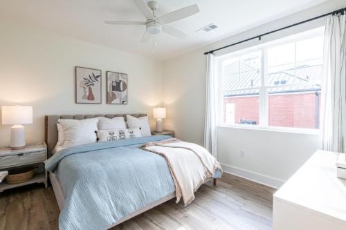 Apartments in for rent Farragut TN A bedroom with a double bed, blue and beige bedding, two bedside tables with lamps, wall art, a ceiling fan, and a window with white curtains. Anchor 934 Apartments in Biddle Farms Town Center