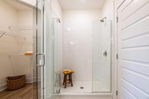 Apartments in for rent Farragut TN A bathroom features a glass-enclosed shower with white tiles and a wooden stool. A wicker basket and wire shelving are visible on the left side. Anchor 934 Apartments in Biddle Farms Town Center