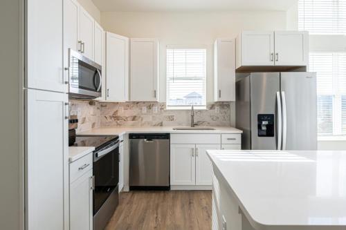 Apartments in for rent Farragut TN Modern kitchen with white cabinets, stainless steel appliances, and a marble backsplash. Natural light streams in through the window above the sink, illuminating the wooden floor. Anchor 934 Apartments in Biddle Farms Town Center