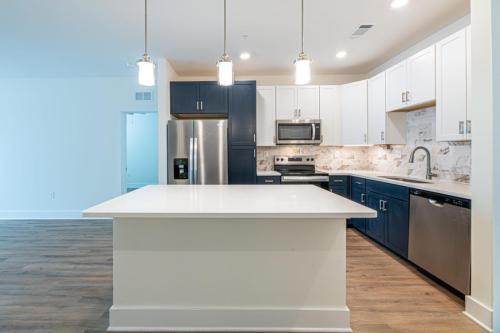 Apartments in for rent Farragut TN Modern kitchen with white and navy cabinets, stainless steel appliances, and a large island. Wood flooring and pendant lights enhance the space. Anchor 934 Apartments in Biddle Farms Town Center