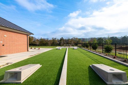 Apartments in for rent Farragut TN Outdoor bocce ball court with artificial turf, concrete borders, and a brick building to the side under a blue sky. Anchor 934 Apartments in Biddle Farms Town Center