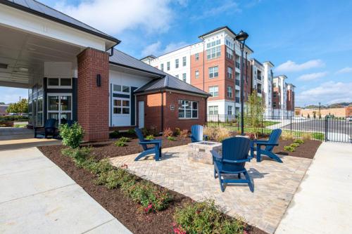 Apartments in for rent Farragut TN Outdoor seating area with blue chairs around a fire pit in front of a modern red brick building and a multi-story apartment complex in the background. Anchor 934 Apartments in Biddle Farms Town Center