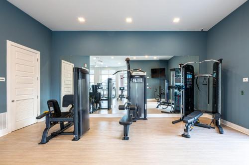 Apartments in for rent Farragut TN A modern gym room with blue walls, mirrored wall, and fitness equipment including a leg press, bench, and cable machine on a wooden floor. Anchor 934 Apartments in Biddle Farms Town Center