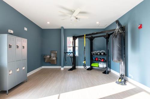 Apartments in for rent Farragut TN A small home gym with blue walls, equipped with lockers, a water fountain, a punching bag, weights, and a TRX system under a ceiling fan. Anchor 934 Apartments in Biddle Farms Town Center