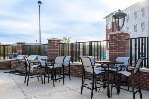 Apartments in for rent Farragut TN Outdoor patio with tables and chairs, a grill, and brick fencing. Building and streetlights in the background under a partly cloudy sky. Anchor 934 Apartments in Biddle Farms Town Center