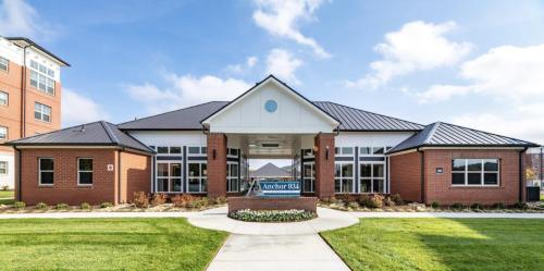 Apartments in for rent Farragut TN A brick building with a triangular roof, large windows, and a manicured lawn, labeled Anchor 943. Anchor 934 Apartments in Biddle Farms Town Center