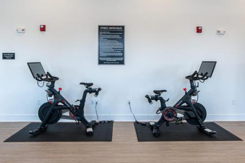 Apartments in for rent Farragut TN Two stationary exercise bikes with screens on mats in a fitness center. A sign with rules is mounted on the wall between them. Anchor 934 Apartments in Biddle Farms Town Center