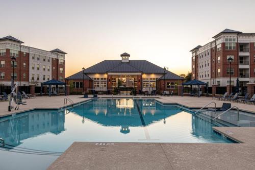 Apartments in for rent Farragut TN Outdoor swimming pool with surrounding lounge chairs and umbrellas, flanked by multi-story brick buildings at sunset. Anchor 934 Apartments in Biddle Farms Town Center