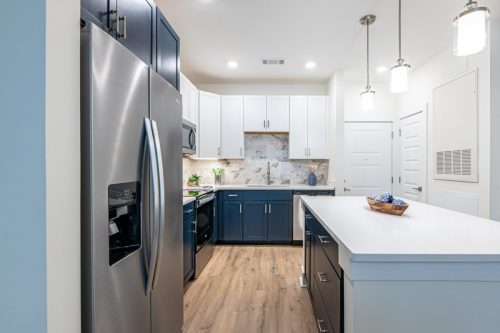 Apartments in for rent Farragut TN Modern kitchen with stainless steel appliances, white and navy cabinets, marble backsplash, island with sink, and wood flooring under bright pendant lights. Anchor 934 Apartments in Biddle Farms Town Center