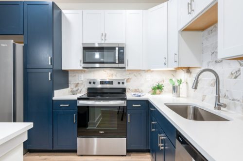 Apartments in for rent Farragut TN Modern kitchen with blue and white cabinets, stainless steel appliances, an electric stove, microwave, and a sink with a gooseneck faucet. Marble backsplash and under-cabinet lighting. Anchor 934 Apartments in Biddle Farms Town Center