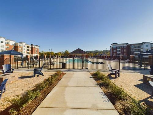 Apartments in for rent Farragut TN View of a gated outdoor pool surrounded by lounge chairs, brick pathway, and residential buildings under a clear blue sky. Anchor 934 Apartments in Biddle Farms Town Center