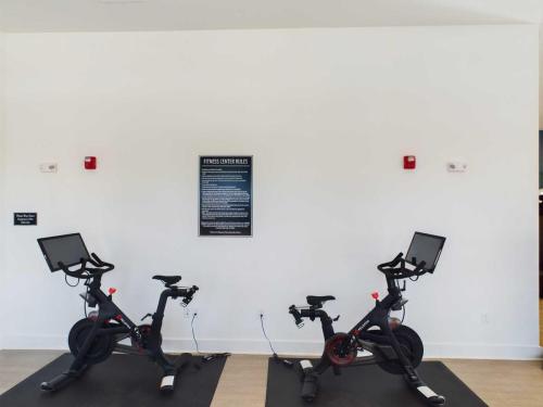 Apartments in for rent Farragut TN Two stationary exercise bikes on mats face a wall with a Fitness Center Rules sign. Red emergency buttons are mounted on the white wall. Anchor 934 Apartments in Biddle Farms Town Center