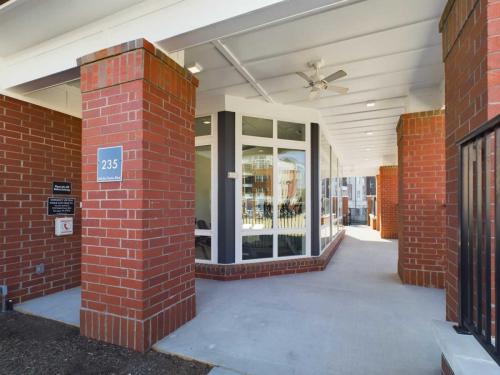 Apartments in for rent Farragut TN Covered walkway with red brick columns and a ceiling fan, leading to a glass windowed area. Sign on a column reads 235. Anchor 934 Apartments in Biddle Farms Town Center