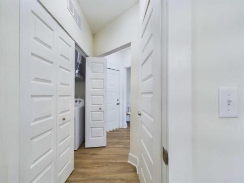 Apartments in Farragut View of a hallway with white doors, one open to reveal a laundry area with a washing machine and dryer. The space features hardwood flooring and white walls. A light switch is visible in the foreground.