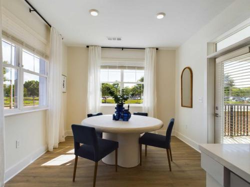Apartments in Farragut A dining area with a white round table, surrounded by four dark blue chairs, a blue centerpiece, and large windows with white curtains allowing natural light to enter the room.