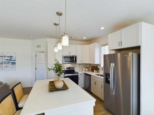 Apartments in Farragut Modern kitchen with white cabinets, stainless steel appliances, and an island with pendant lights. A potted plant and wicker chairs are on the island, and a sofa is visible in the background.