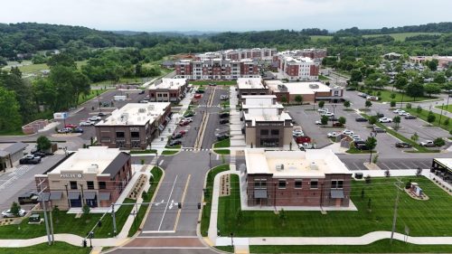 Biddle Farms Farragut Town Center Apartments in for rent Farragut TN Aerial view of Biddle Farms Farragut Town Center shows a modern commercial plaza with multiple brick buildings, parking lots, green spaces, and residential buildings in the background. Anchor 934 Apartments in Biddle Farms Town Center