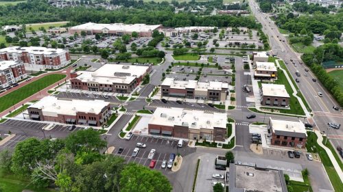 Apartments in for rent Farragut TN Aerial view of Biddle Farms Farragut Town Center, showcasing multiple commercial buildings, parking lots, roads, green spaces, and surrounding trees along a main road. Anchor 934 Apartments in Biddle Farms Town Center
