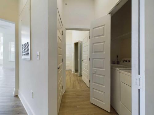 Apartments in for rent Farragut TN A hallway in a modern home with multiple doors, including a partially open door revealing a laundry area with a washer and dryer. The flooring is light wood, and the walls are painted white. Anchor 934 Apartments in Biddle Farms Town Center