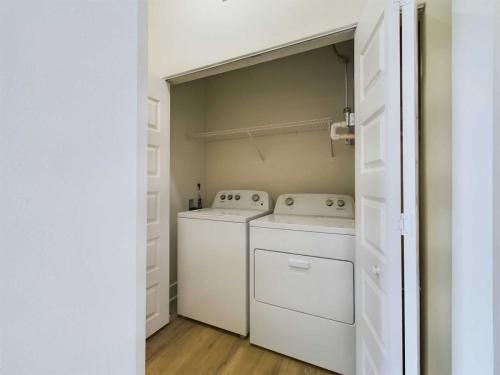 Apartments in for rent Farragut TN White washing machine and dryer set in a small laundry closet with open bi-fold doors and an overhead shelf on a wooden floor. Anchor 934 Apartments in Biddle Farms Town Center