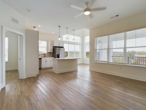 Apartments in for rent Farragut TN A spacious open-plan kitchen and living area with hardwood floors, large windows, and a ceiling fan. The kitchen includes modern appliances and a central island with pendant lighting. Anchor 934 Apartments in Biddle Farms Town Center