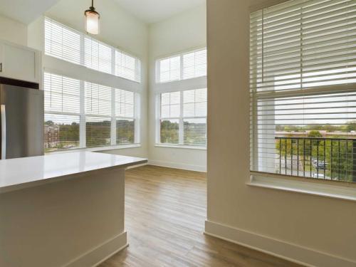 Apartments in for rent Farragut TN A bright, empty room with large windows, wooden flooring, and white walls. A kitchen counter is partially visible on the left. Anchor 934 Apartments in Biddle Farms Town Center