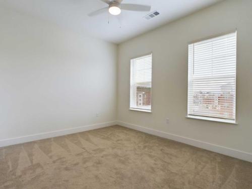 Apartments in for rent Farragut TN Empty room with beige carpet, white walls, and two large windows with blinds. A ceiling fan is centered above. Anchor 934 Apartments in Biddle Farms Town Center