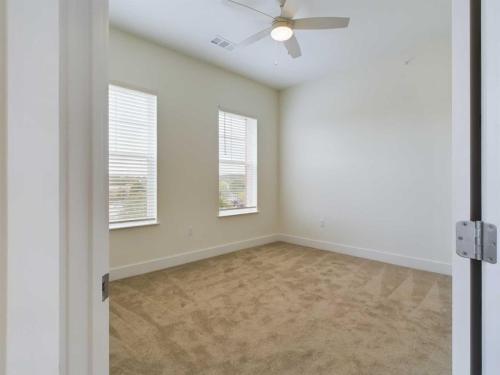 Apartments in for rent Farragut TN Empty room with beige carpet, white walls, two windows with blinds, and a ceiling fan. Anchor 934 Apartments in Biddle Farms Town Center