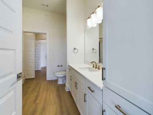 Apartments in for rent Farragut TN A modern bathroom with white cabinets, double sinks, large mirror, and wood-look flooring. A toilet is visible in the adjoining area. Anchor 934 Apartments in Biddle Farms Town Center