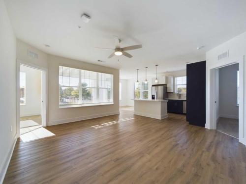 Apartments in for rent Farragut TN An empty modern apartment with hardwood floors, large windows, a ceiling fan, and an open kitchen with pendant lights. Anchor 934 Apartments in Biddle Farms Town Center