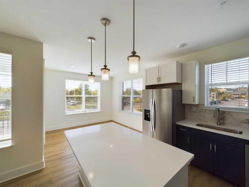 Apartments in for rent Farragut TN Bright modern kitchen with large windows, hardwood flooring, stainless steel fridge, pendant lights, and a marble countertop island. Anchor 934 Apartments in Biddle Farms Town Center