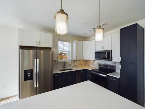 Apartments in for rent Farragut TN Modern kitchen with white and black cabinets, stainless steel refrigerator, oven, and microwave, marble backsplash, and two pendant lights over a white island. Anchor 934 Apartments in Biddle Farms Town Center