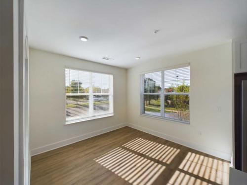 Apartments in for rent Farragut TN A sunlit room with large windows, white walls, and wooden flooring. Shadows cast by the window blinds create patterns on the floor. Anchor 934 Apartments in Biddle Farms Town Center