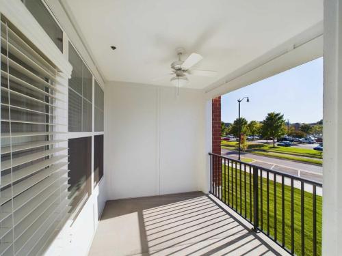 Apartments in for rent Farragut TN A covered balcony features a ceiling fan, black railing, and a view of parked cars and trees on a sunny day. Anchor 934 Apartments in Biddle Farms Town Center