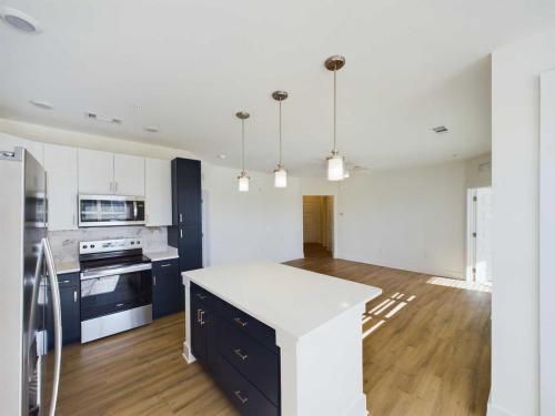 Apartments in for rent Farragut TN Modern kitchen with white cabinets, a dark kitchen island, stainless steel appliances, and wood flooring. Three pendant lights hang above the island. Anchor 934 Apartments in Biddle Farms Town Center