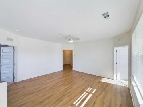 Apartments in for rent Farragut TN An empty room with wooden flooring, white walls, and large windows. There is a ceiling fan and several closed white doors. Natural light illuminates the space. Anchor 934 Apartments in Biddle Farms Town Center