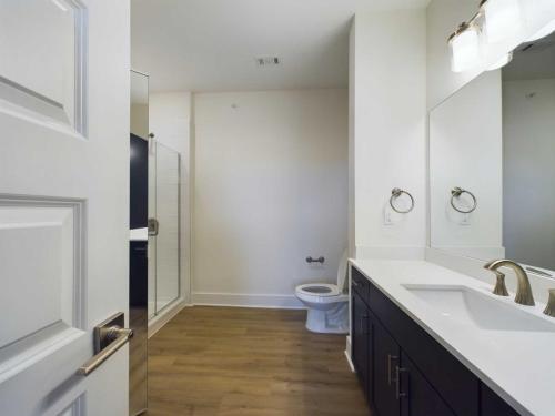 Apartments in for rent Farragut TN Modern bathroom with wooden floor, a large mirror, dual-sink vanity, toilet, and glass-enclosed shower. Anchor 934 Apartments in Biddle Farms Town Center