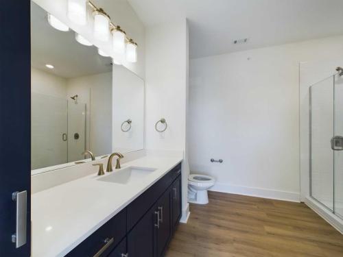 Apartments in for rent Farragut TN Modern bathroom with a large mirror, double sink, dark cabinetry, and wooden flooring. Glass-enclosed shower visible in the background. Anchor 934 Apartments in Biddle Farms Town Center